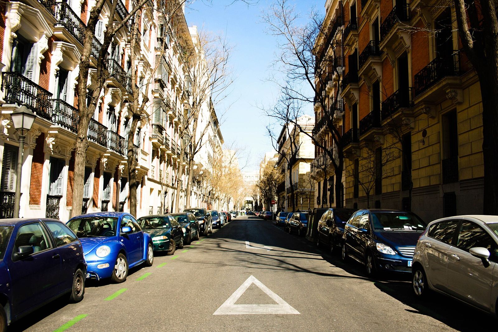 Calle de un barrio de Madrid con edificios de ladrillo y balcones y coches aparcados a ambos lados